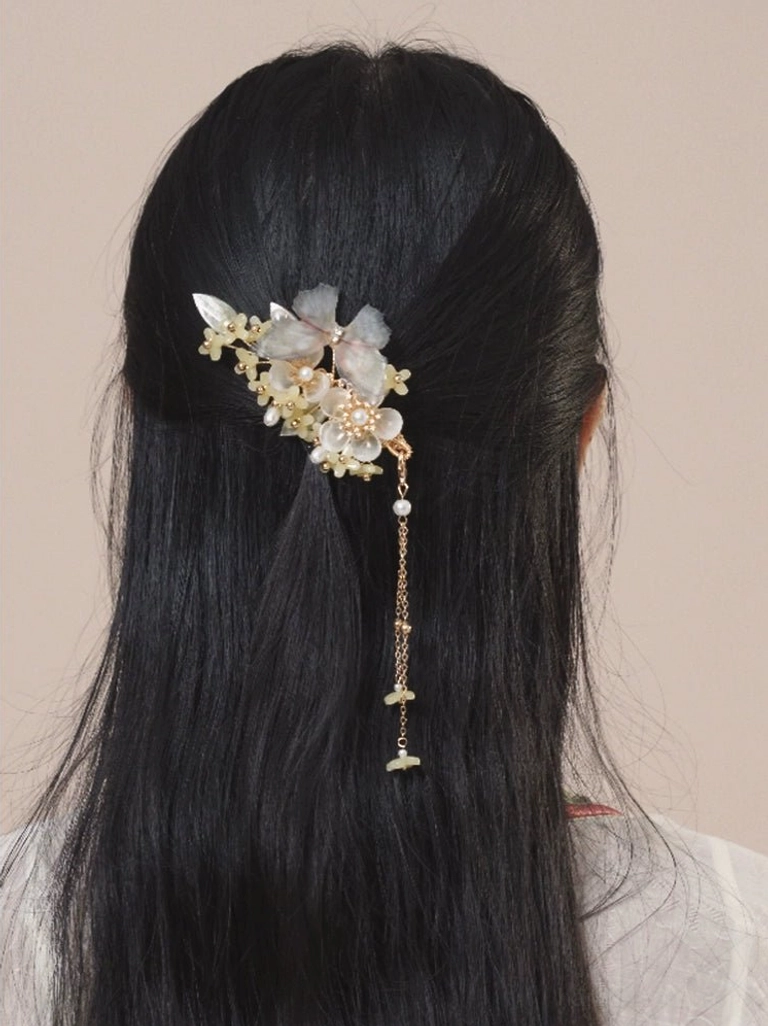 Cream floral Hanfu hair clip with green leaves, pearl bead accents, and a long gold-tone tassel worn in long black hair