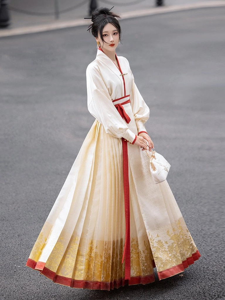 Front view of a model wearing a cream Ming Dynasty Hanfu mamianqun skirt with pleats, metallic floral hem, red trim, white cross-collar top, and red waist sash