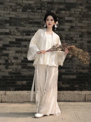 Full body front view of cream Song Dynasty Hanfu set with lace trimmed wide sleeve top and tassel wide-leg pants outdoors