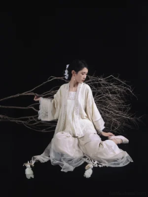 Side view of woman sitting in cream Song style Hanfu outfit with flowing wide-leg pants and rabbit tassel hem details