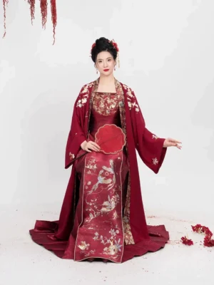 Seated bridal model wearing Crimson Magpie Ming Dynasty Hanfu wedding set with red round fan embroidered mamian skirt and long overcoat