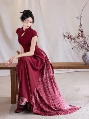 Crimson qipao-style Ao Dai modern Hanfu dress with fitted stand-collar bodice and flowing tie-dye maxi skirt shown in a seated three-quarter view