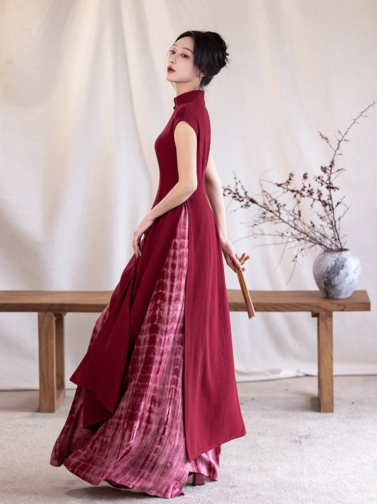 Crimson qipao-style split Ao Dai dress shown from the side with slim waist fit, flowing asymmetric hem, and matching tie-dye under-skirt