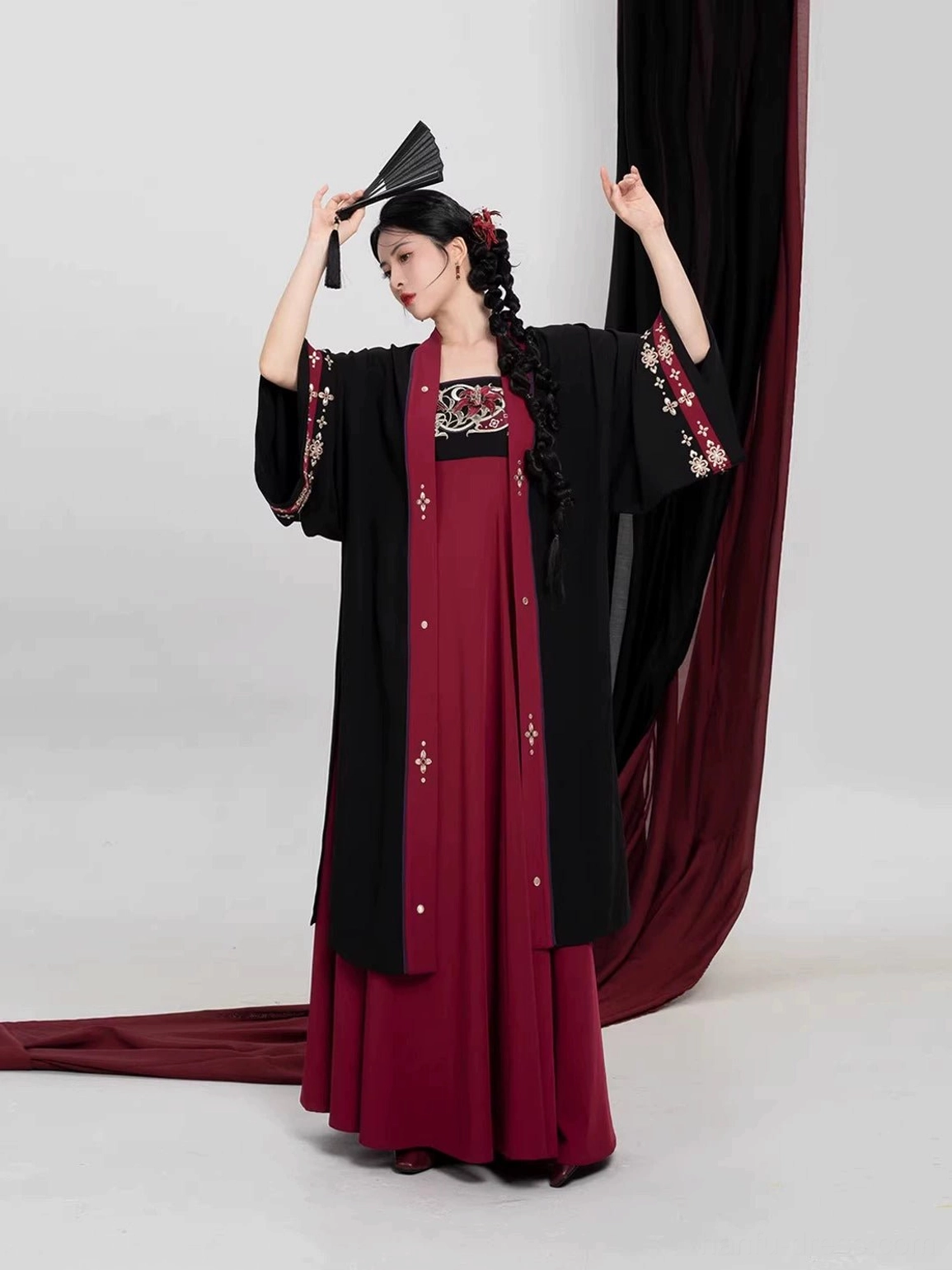 Dynamic three-quarter view of a crimson scarlet Tang Dynasty Hanfu outfit with flowing A-line slip dress, embroidered cuffs, and long black open-front jacket