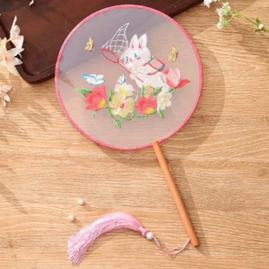 Cute kitten and flower embroidered traditional Chinese round hand fan with pink trim bamboo handle white bead and pink tassel displayed on a wooden table