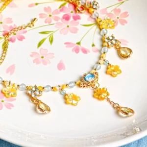Hanfu yingluo forehead chain and Chinese necklace jewelry set displayed on a pink cherry blossom ceramic plate with gold-tone chains, yellow flowers, faux pearls, blue gems, and teardrop pendants