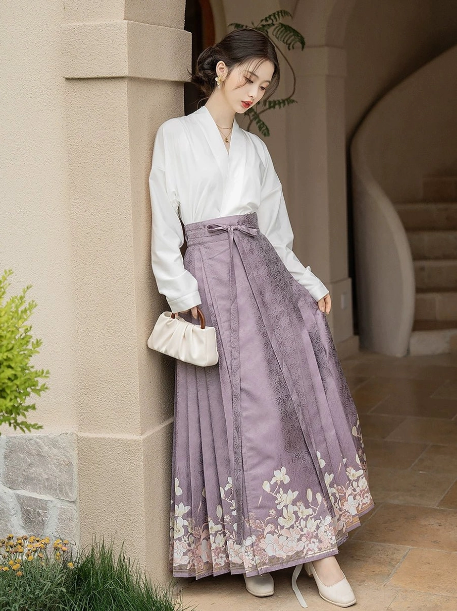 Daily wear Hanfu outfit shown from the right side with a white cross-collar blouse, flowing dusty purple mamianqun horse face skirt, floral hem prints, and white mini handbag