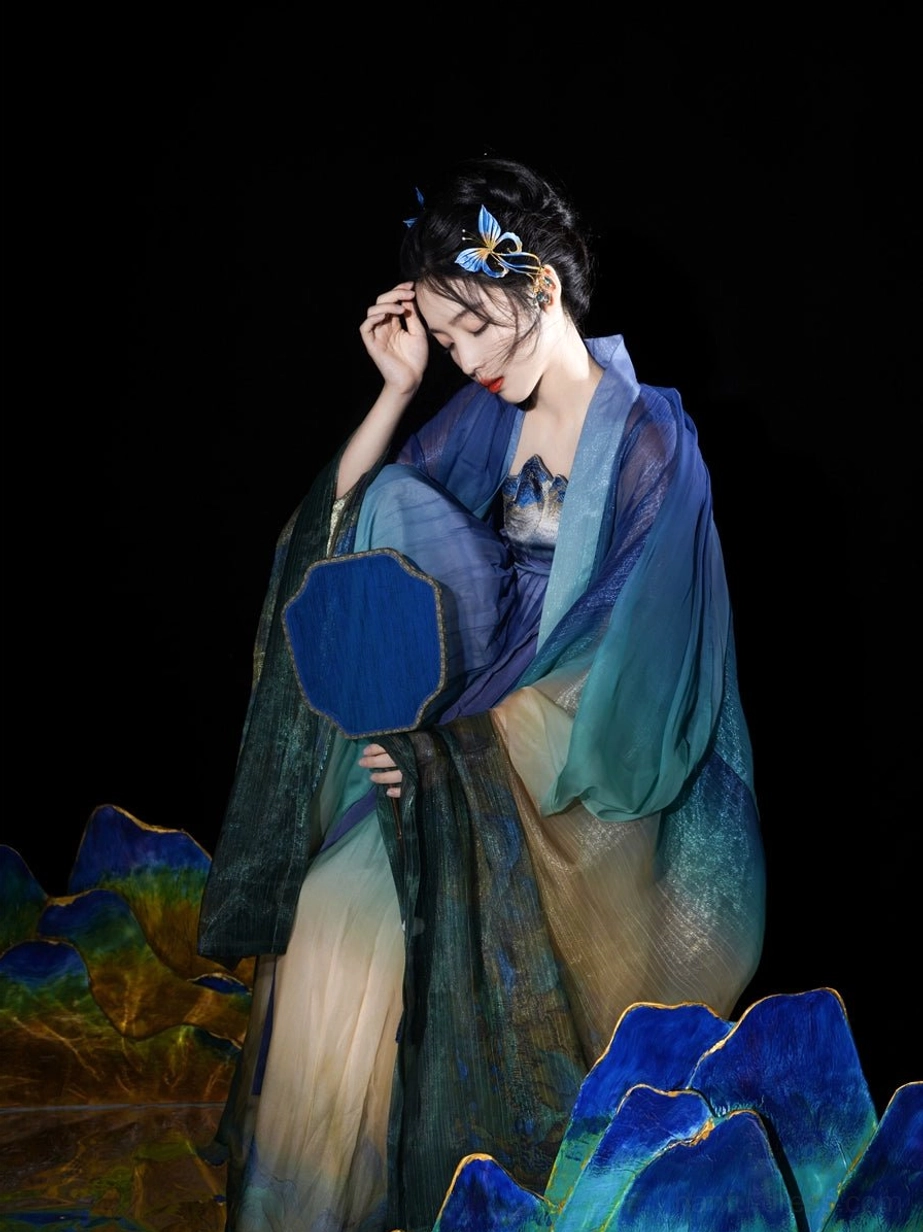 Elegant front three quarter view of a Daisy Blue Tang Dynasty Heziqun Hanfu with navy sheer coat gradient skirt and fan