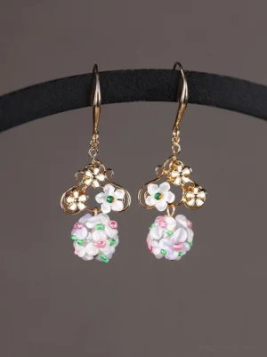Daisy fairy floral dangle earrings with gold tone flower tops and pastel bead cluster pendants displayed on a black velvet jewelry stand