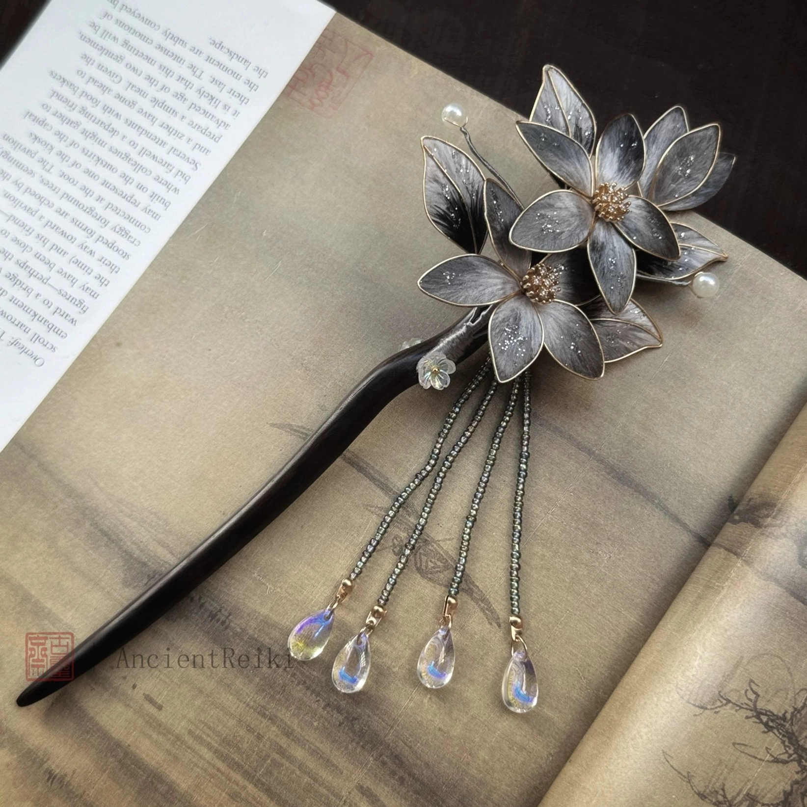 Front view of Danqing handmade Chinese hair stick on an open printed book, highlighting the lotus floral decoration, pearl beads and iridescent tassel drops