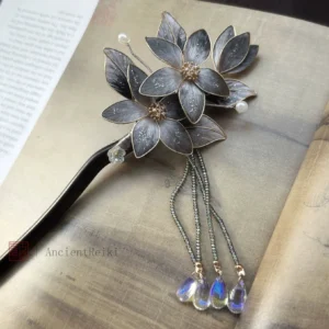 Top view of Danqing traditional Chinese hair stick with dark lotus flower cluster, pearl accents, beaded tassels and blue iridescent teardrop charms on a vintage book