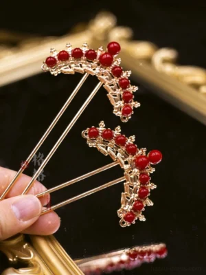 Danxia red bead Chinese Hanfu hair pins held in hand, featuring gold-toned crown-shaped metal frames and long hair stick shafts