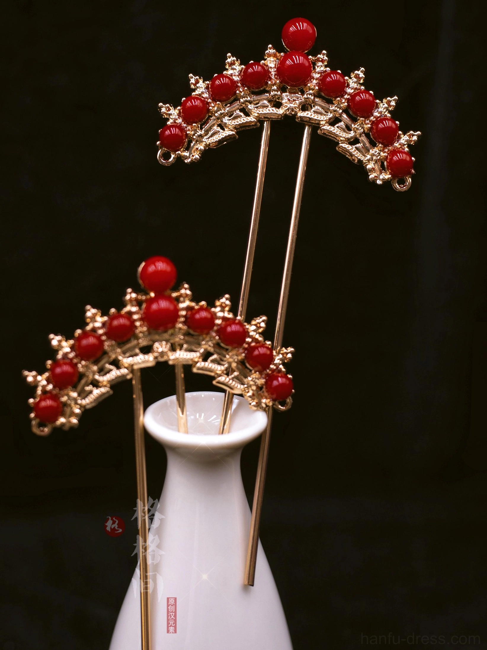 Pair of red and gold Chinese bridal hair pins displayed on a white porcelain vase against a black background