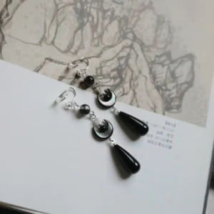 Dark crescent Chinese Hanfu clip-on drop earrings with black teardrop pendants displayed on a traditional Chinese landscape painting page
