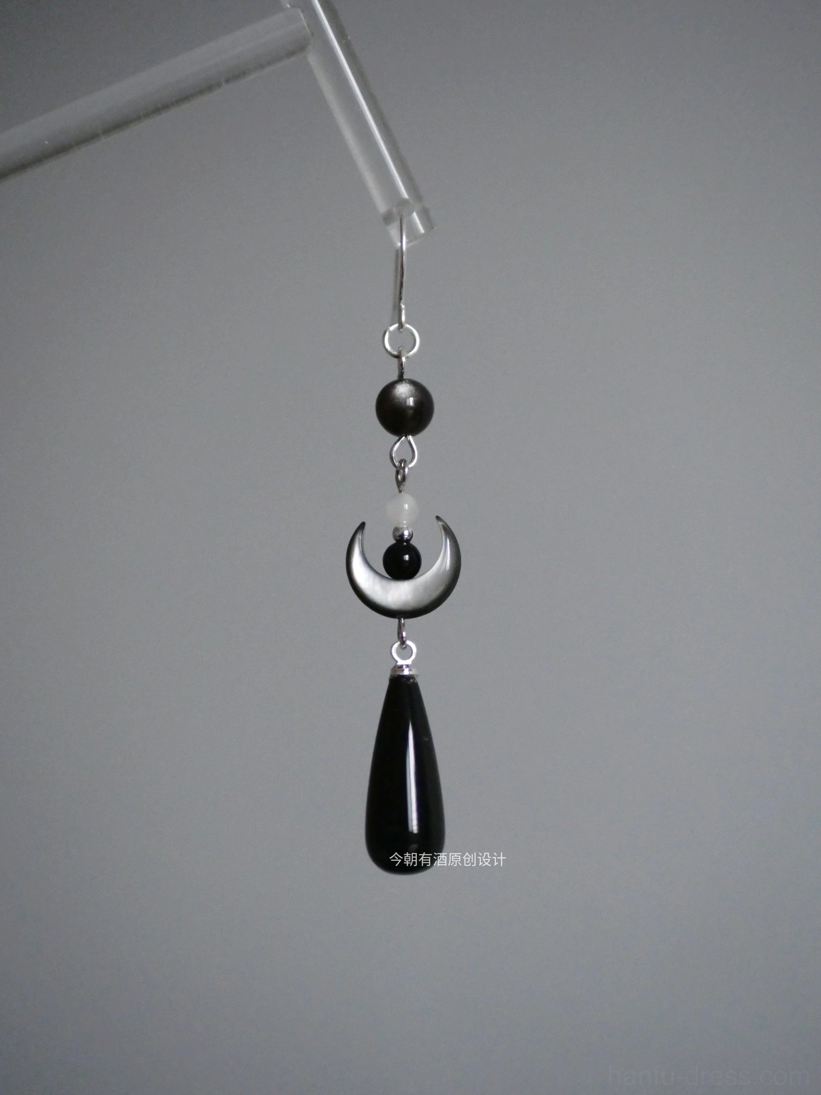 Close-up of dark crescent Chinese Hanfu drop earring with silver hook black round bead pale accent bead crescent charm and black pendant
