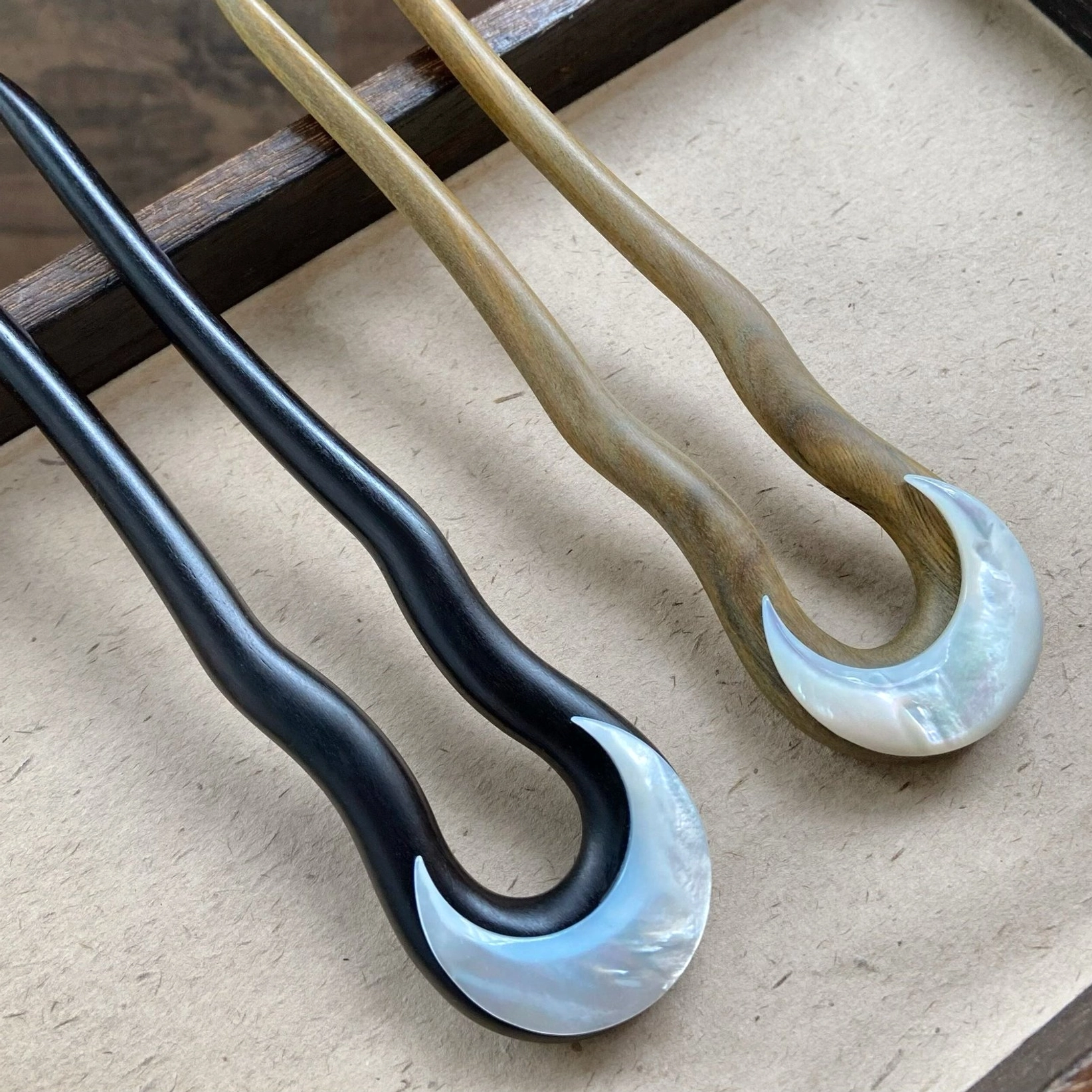 Dark matte black crescent moon Chinese hair stick with iridescent mother-of-pearl inlay displayed on a linen-covered wooden tray