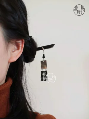 Woman wearing a dark wood Chinese hair stick with black beaded tassel pendant in a low bun, Hanfu-inspired hairstyle accessory shown from the side