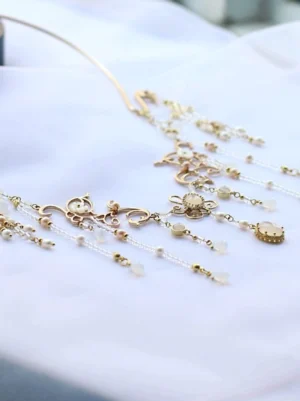 Chinese-style gold collar necklace shown in a flat lay with floral filigree accents, oval pendants, multiple beaded tassel chains, and white decorative beads