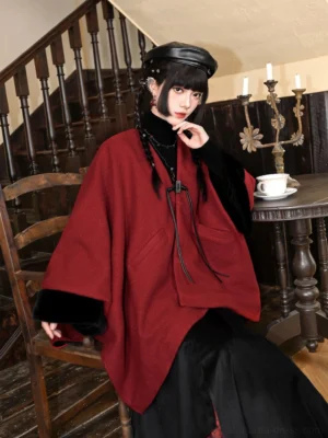 Deep red New Chinese style winter cape with frog buckle closures and black fuzzy cuffs, shown in a three-quarter seated front view