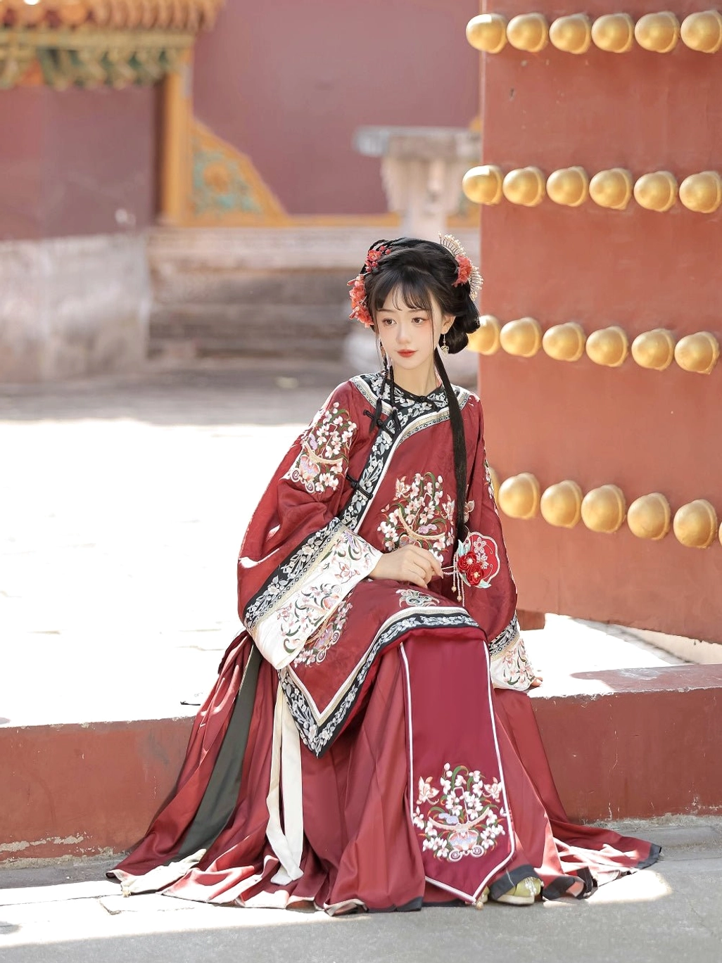 Deep red Qing Dynasty Han women's traditional blouse and skirt styling with floral embroidery, white sleeve borders, and red Chinese hair accessories