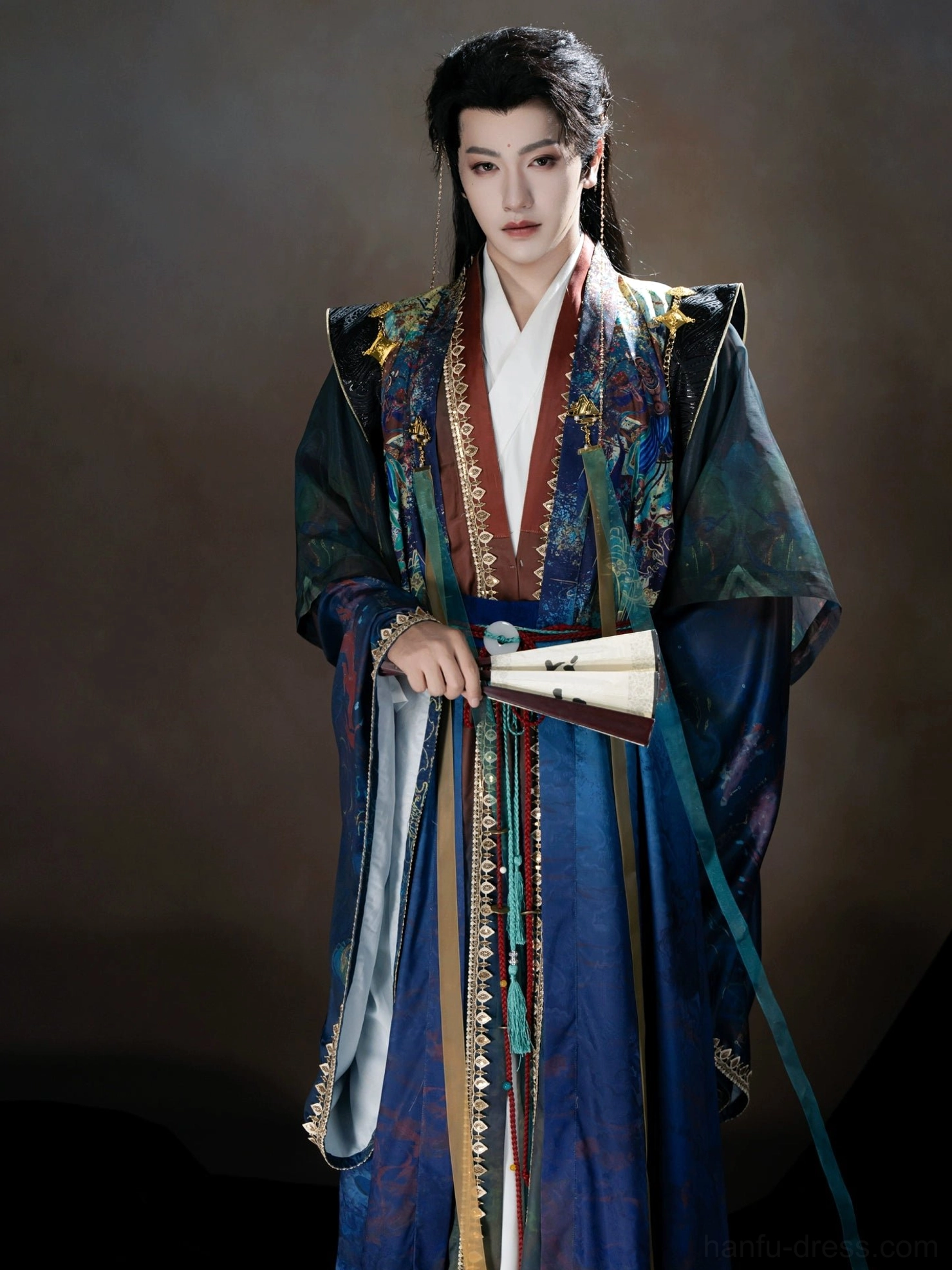 Full-body front view of a male Demon Prince of Dunhuang Xianxia Hanfu costume with sweeping blue robes, gilded trim, landscape chest artwork, waist tassels, and folding fan styling