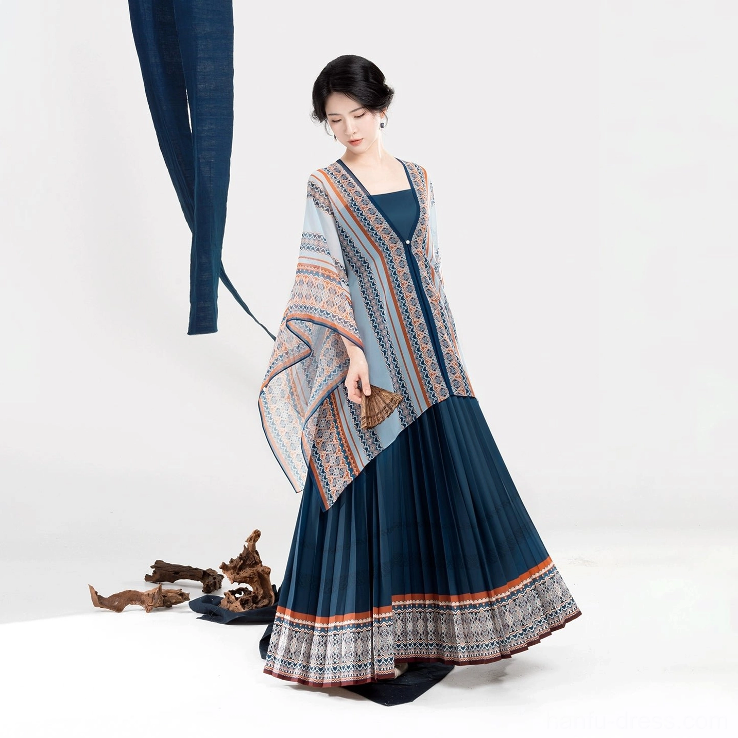 Front low-angle view of a Dong-inspired Chinese-style dress set with neatly draped light blue shawl, dark blue pleated skirt, and wooden fan