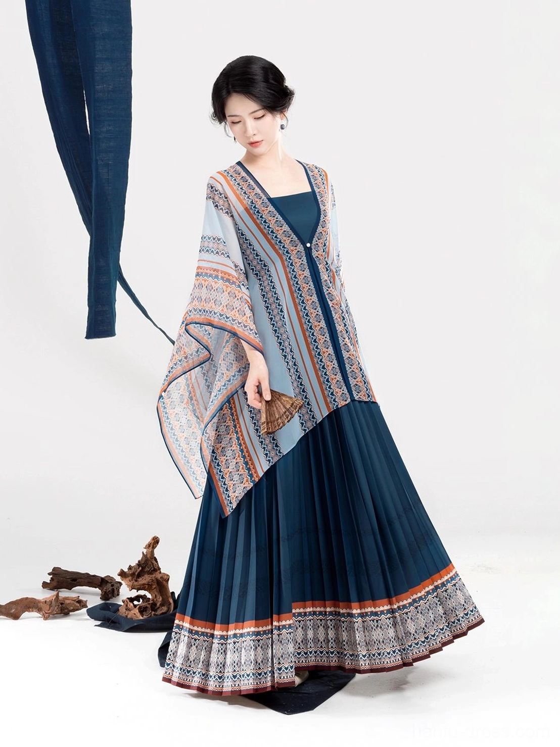Front full-body view of a Dong-inspired modern Hanfu dress set with light blue geometric shawl, dark blue pleated skirt, and ethnic-style hem trim