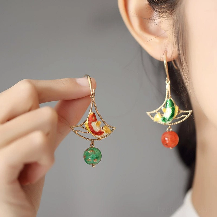 Woman wearing asymmetric koi fish cheongsam earrings with gold hooks and colorful glass bead pendants in a close-up lifestyle view