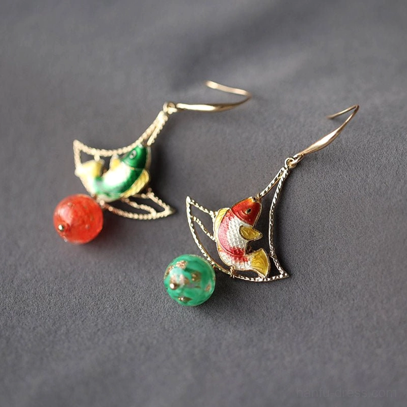 Pair of mismatched koi fish drop earrings on gray fabric showing fine gold ear wires, colorful fish charms, and coordinating red and green bead drops