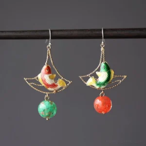 Mismatched Double Blessing koi fish earrings with reversed red and green enamel-style carp designs hanging from a black display rod