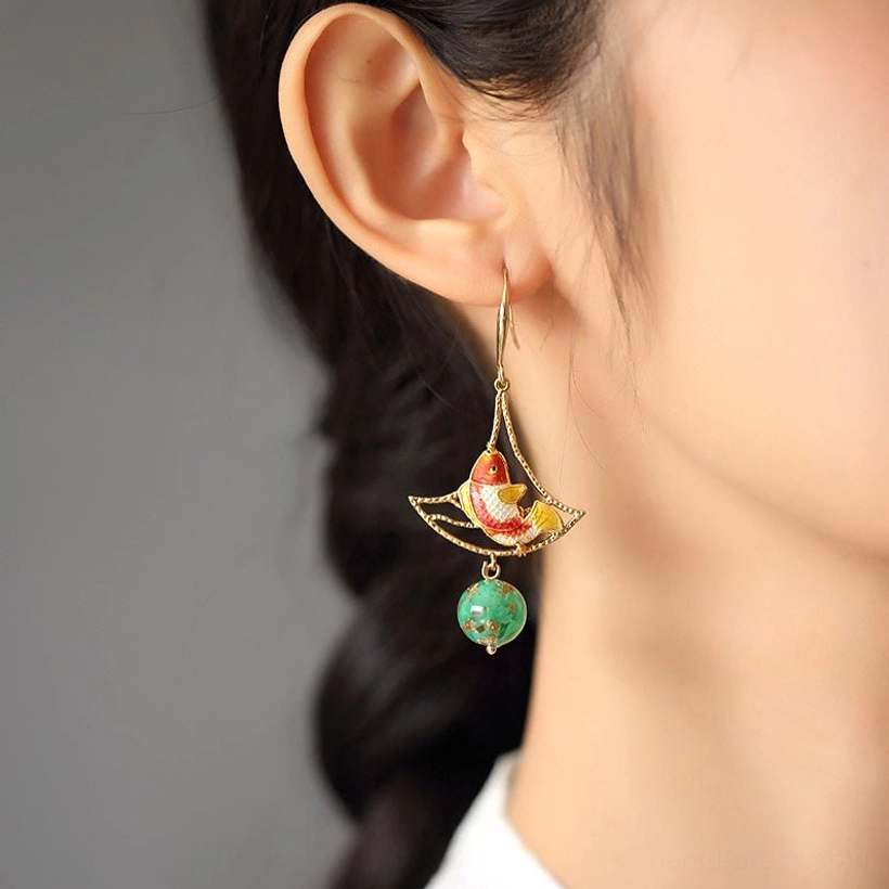 Close-up profile of a woman wearing a red koi fish earring with a gold filigree frame and green speckled dangling bead
