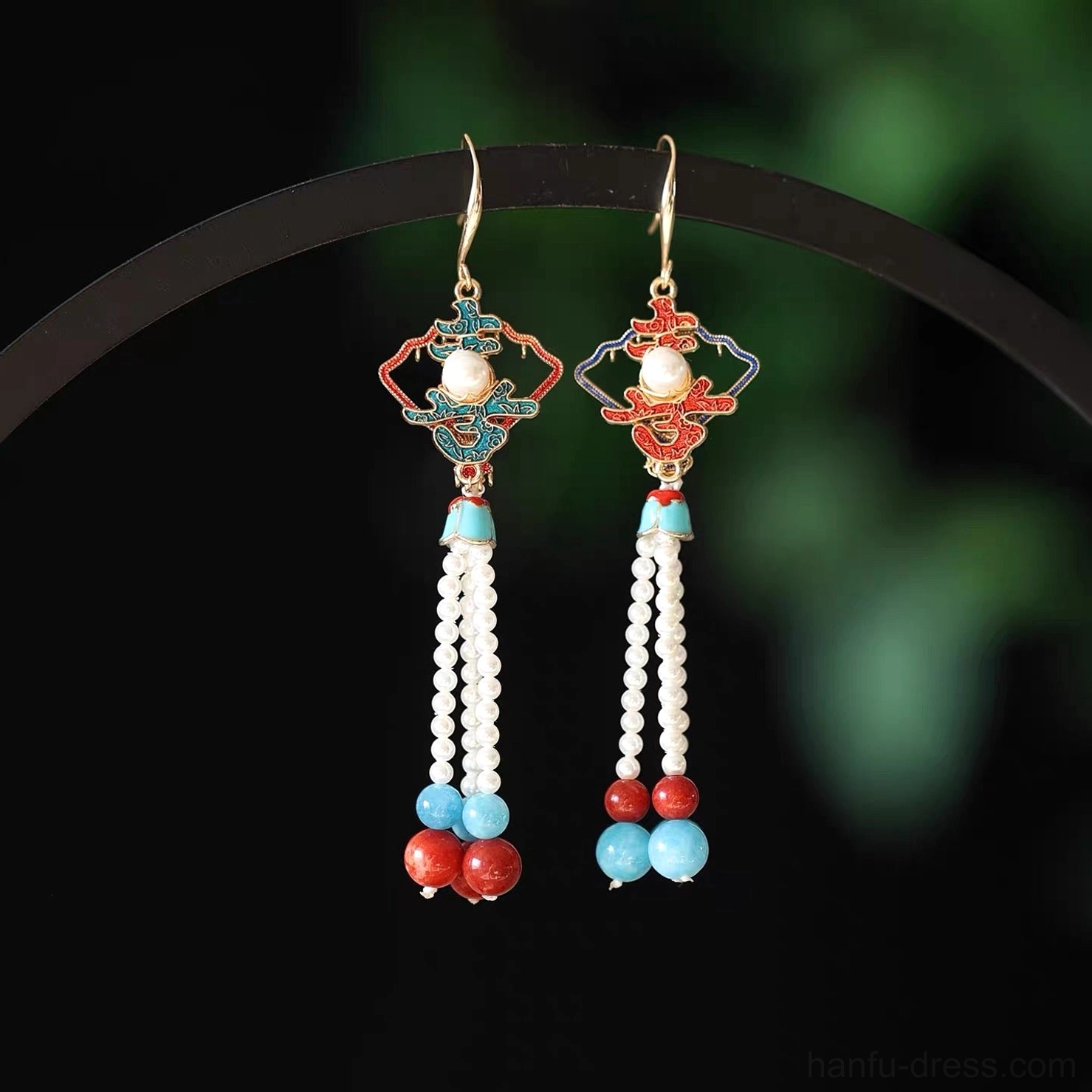 Pair of traditional Chinese tassel drop earrings displayed on a black jewelry hanger with gold ear wires, colorful enamel tops, pearl tassels, and red blue beads