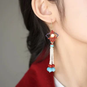 Model wearing traditional Chinese Double Happiness tassel earrings with gold hook, enamel ornament, central pearl, pearl tassel, and red and blue bead pendants