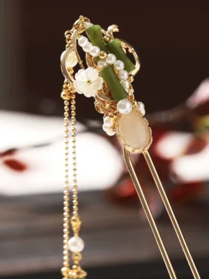 Top-front view of a double-pronged bamboo Chinese hair stick featuring green bamboo accents, white floral beads, clustered faux pearls, gold-tone hardware, and decorative tassel elements