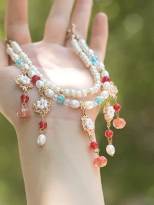 Close-up of a double-strand vintage Chinese necklace resting on a hand, decorated with pearl chains, gold flower pendants, red beads, colorful charms, and freshwater pearl drops