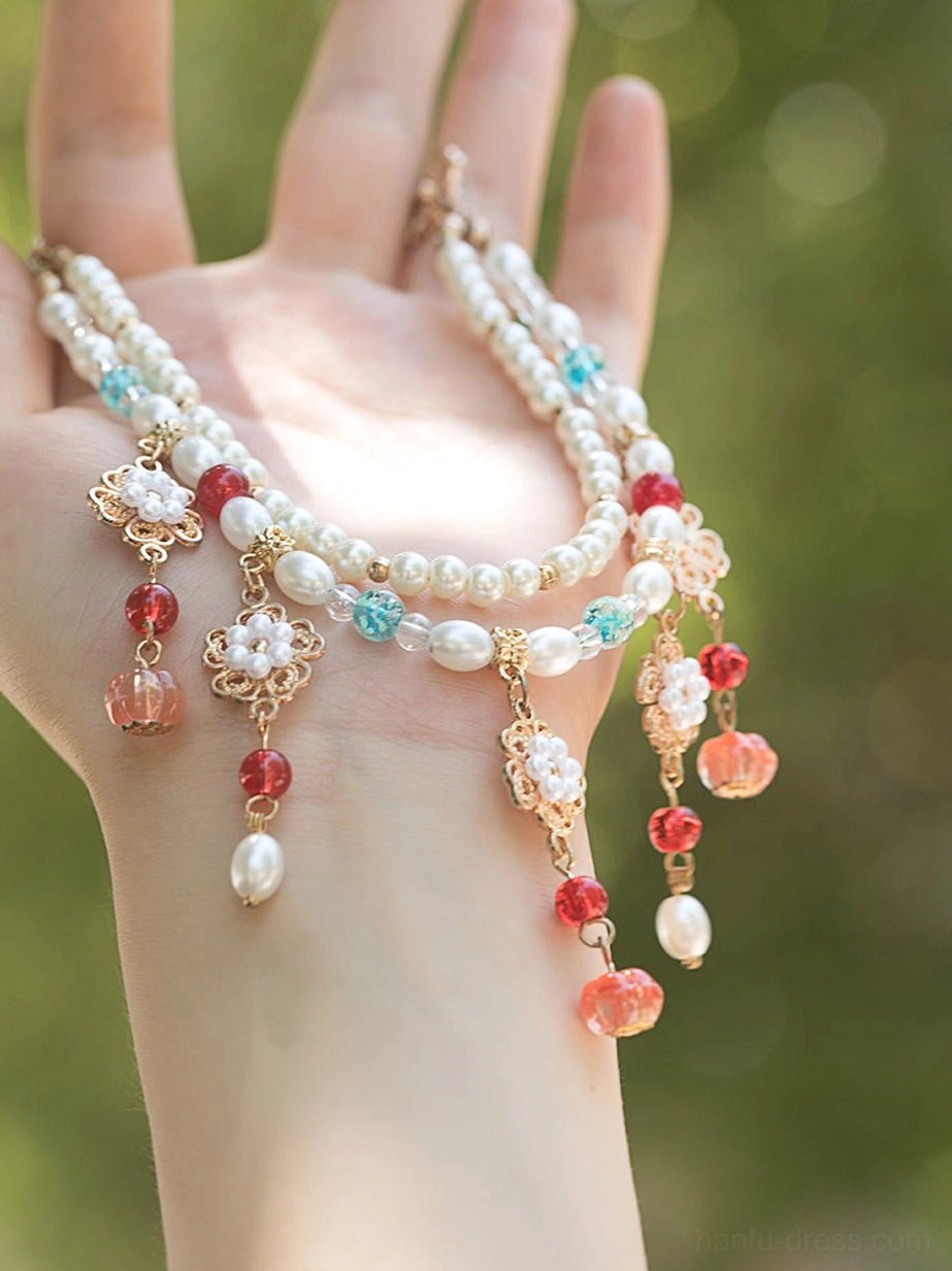 Close-up of a double-strand vintage Chinese necklace resting on a hand, decorated with pearl chains, gold flower pendants, red beads, colorful charms, and freshwater pearl drops