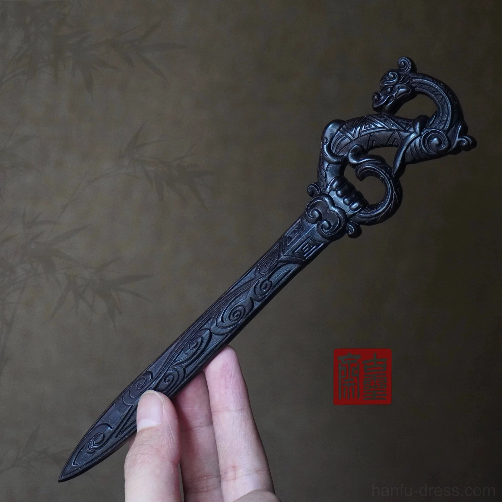 Hand holding a long dragon carved Chinese hair stick showing its full pointed shaft and scale for Hanfu wuxia hairstyles