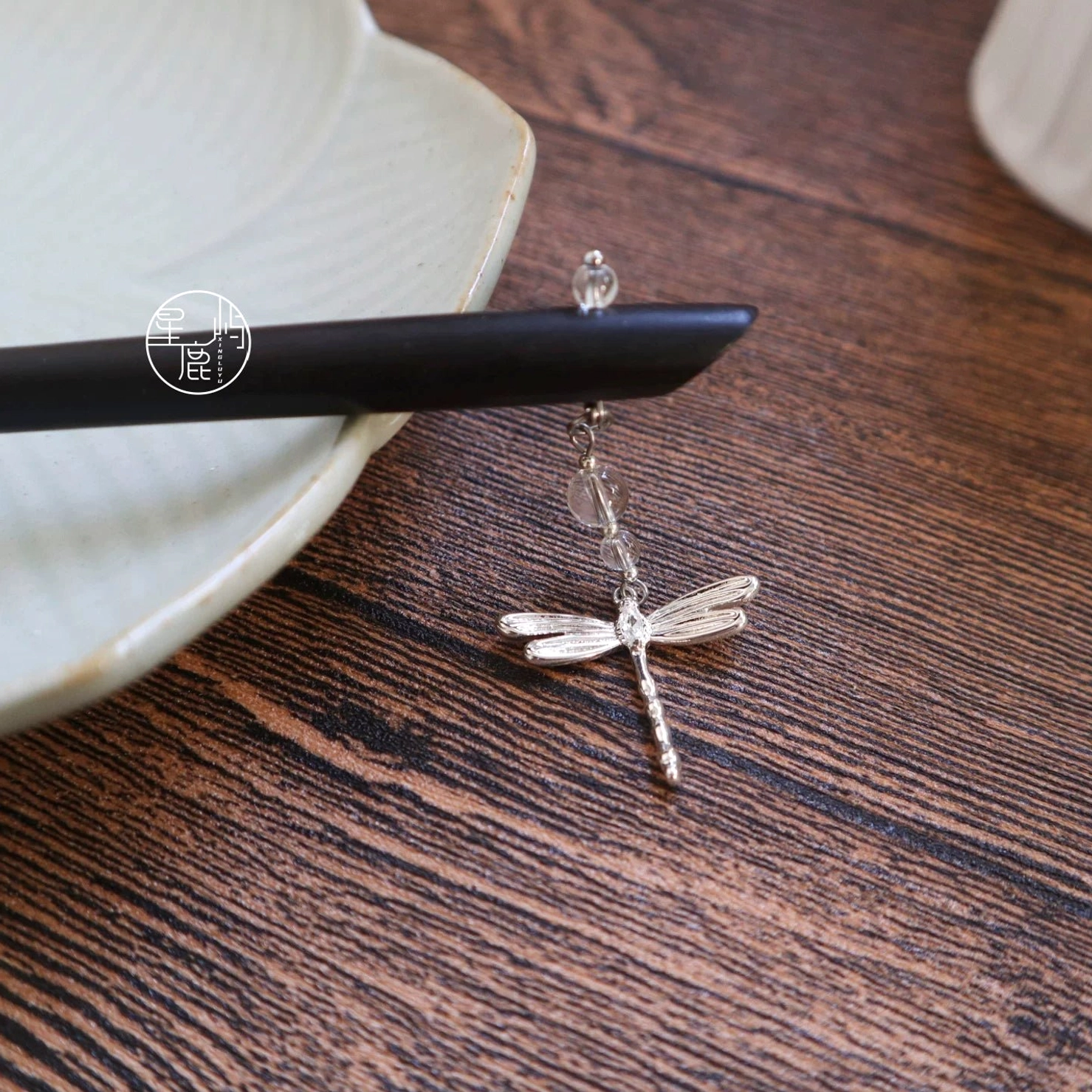 Dragonfly Hanfu hair accessory displayed on a dark wooden table, showing the black wood hair stick, silver-toned dragonfly charm, and delicate beaded hanging chain