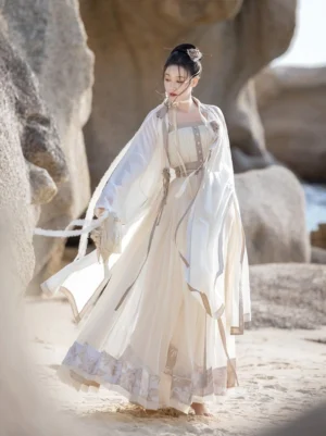 Dream of Mountains Ming Dynasty Hanfu set shown in a full body side view on a rocky coastal beach, featuring a cream white sheer wide sleeve robe, flowing mamian skirt, embroidered ruffled hem, and grey trim details