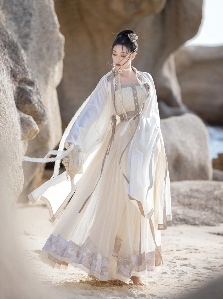 Dream of Mountains Ming Dynasty Hanfu set shown in a full body side view on a rocky coastal beach, featuring a cream white sheer wide sleeve robe, flowing mamian skirt, embroidered ruffled hem, and grey trim details
