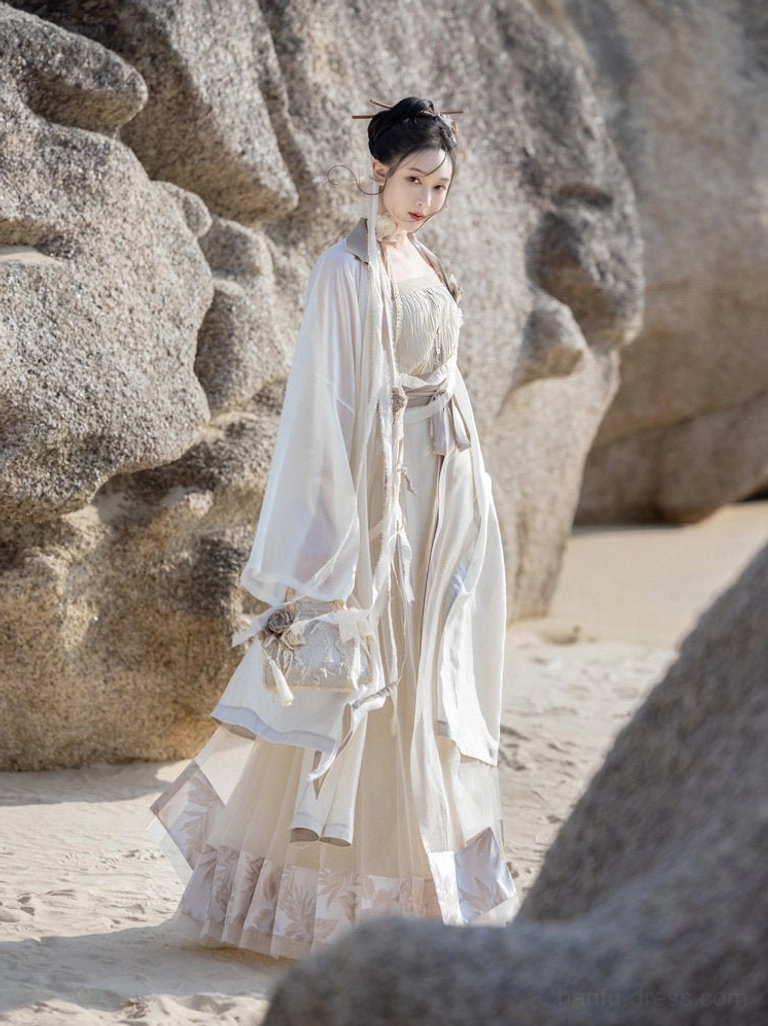 Dream of Mountains Ming inspired Hanfu clothing shown from the side on a rocky beach, featuring traditional Hanfu hair ornaments, woven waist handbag, cream robe, mamian skirt, and grey trim
