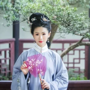 Woman wearing light blue Ming style Hanfu with Dream of Red Mansion phoenix tassel hairpins and purple Chinese folding fan in a traditional garden