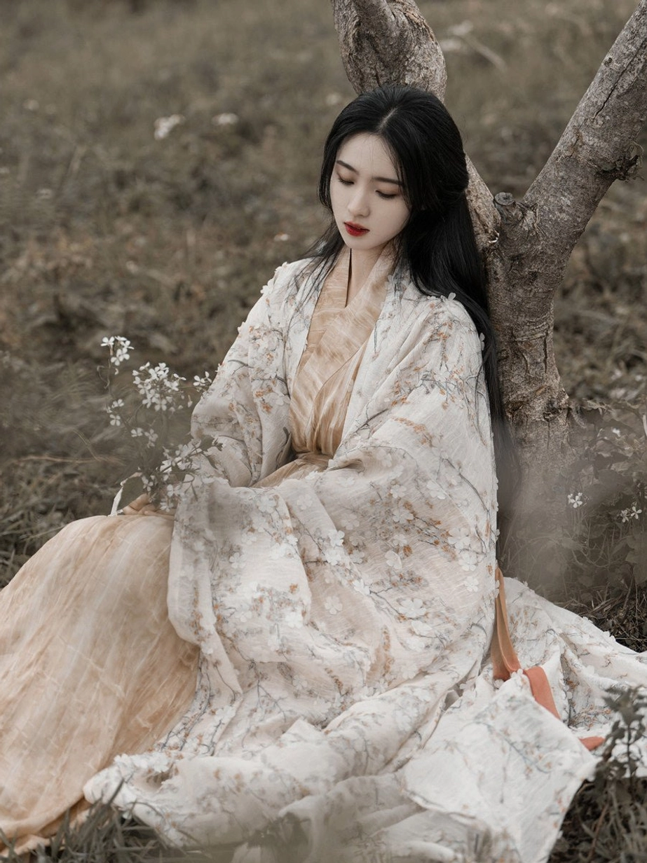 Woman sitting outdoors in a dreamlike Wei Jin Dynasty Qiyao Ruqun Hanfu with floral coat beige inner dress long skirt and orange sash