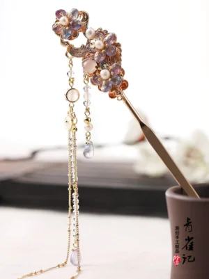 Dreamscape traditional Chinese floral hair stick shown in a dark ceramic cup with purple flower beads, pearl accents, and long tassel chains