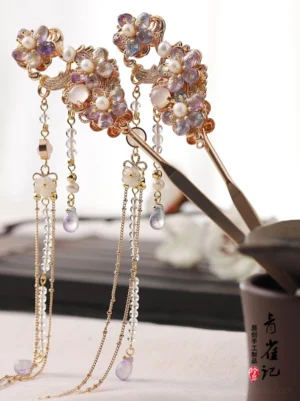 Pair of Dreamscape purple floral tassel Chinese hair sticks with gold-tone settings, pearl-like beads, and teardrop pendants displayed on a dark tray