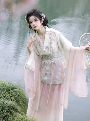 Wei Jin Dynasty Hanfu three quarter view by lakeside featuring embroidered floral waist apron, flowing sleeves, tassel pendants and round fan