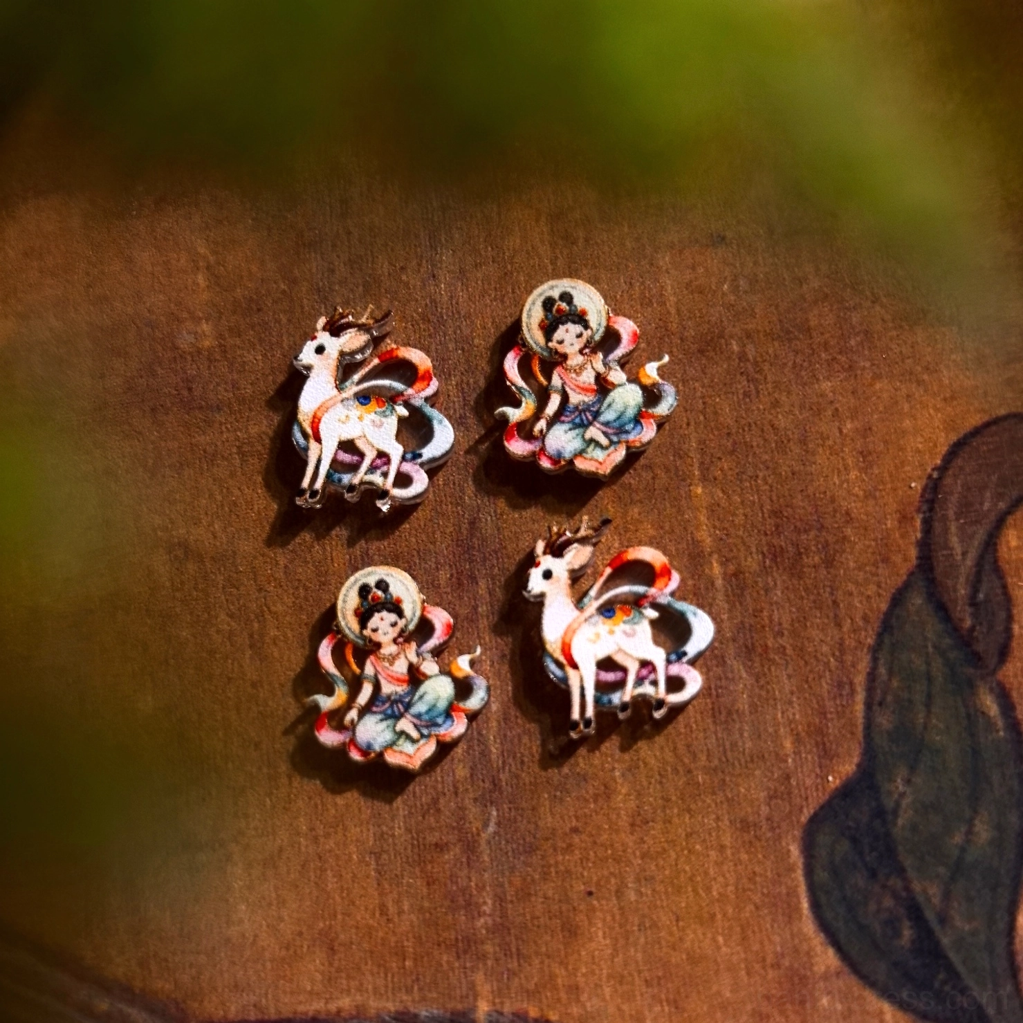 Dunhuang Apsara and Nine-Colored Deer stud earrings with hand-painted Chinese art details displayed on a vintage wooden background with leaf motifs