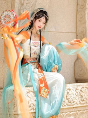 Dunhuang Feitian Tang Dynasty Hanfu dance costume set shown from a low three quarter angle with flowing gauze ribbons, veil, embroidered waist styling, gold accessories, and hand drum prop