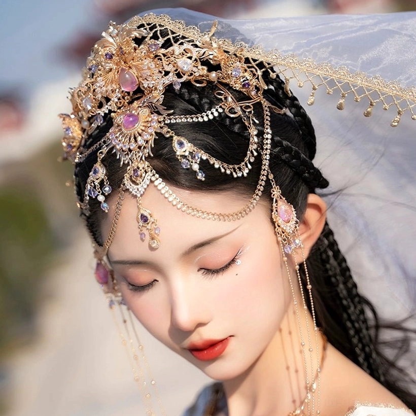 Close-up of a Dunhuang Hanfu forehead crown with ornate gold filigree, pink-purple crystal decorations, and long layered face chain tassels on braided hair