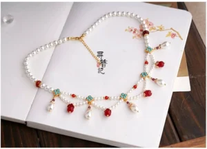 Top-down view of a Dunhuang inspired Chinese necklace with pearl strands, red and turquoise ornaments, gold-tone chain closure, and elegant traditional jewelry details